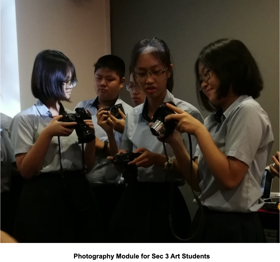 Four students hold cameras and look at them during a photography module class.